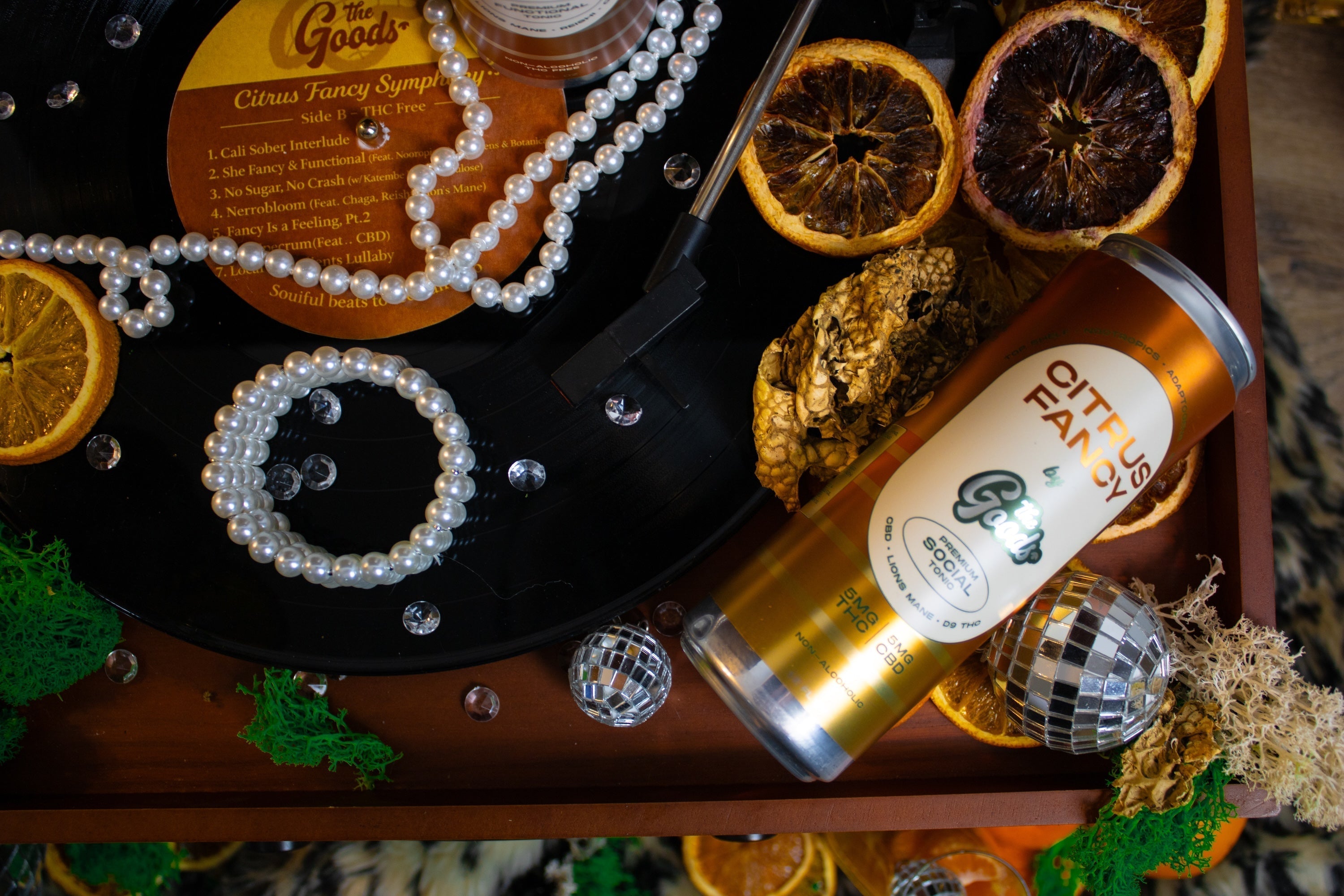 a can of Citrus Fancy The Goods Functional Mushroom Beverage sitting on a table with various branded elements such as sliced oranges and jewelry