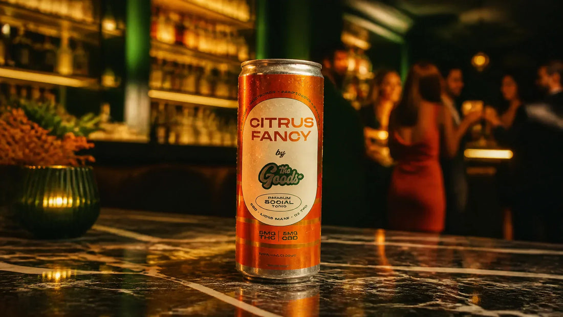 A premium 12oz can of The Goods Citrus Fancy social tonic (5mg THC, 5mg CBD) sitting on a marble table in an elevated, moody social lounge with deep green and vibrant orange lighting.