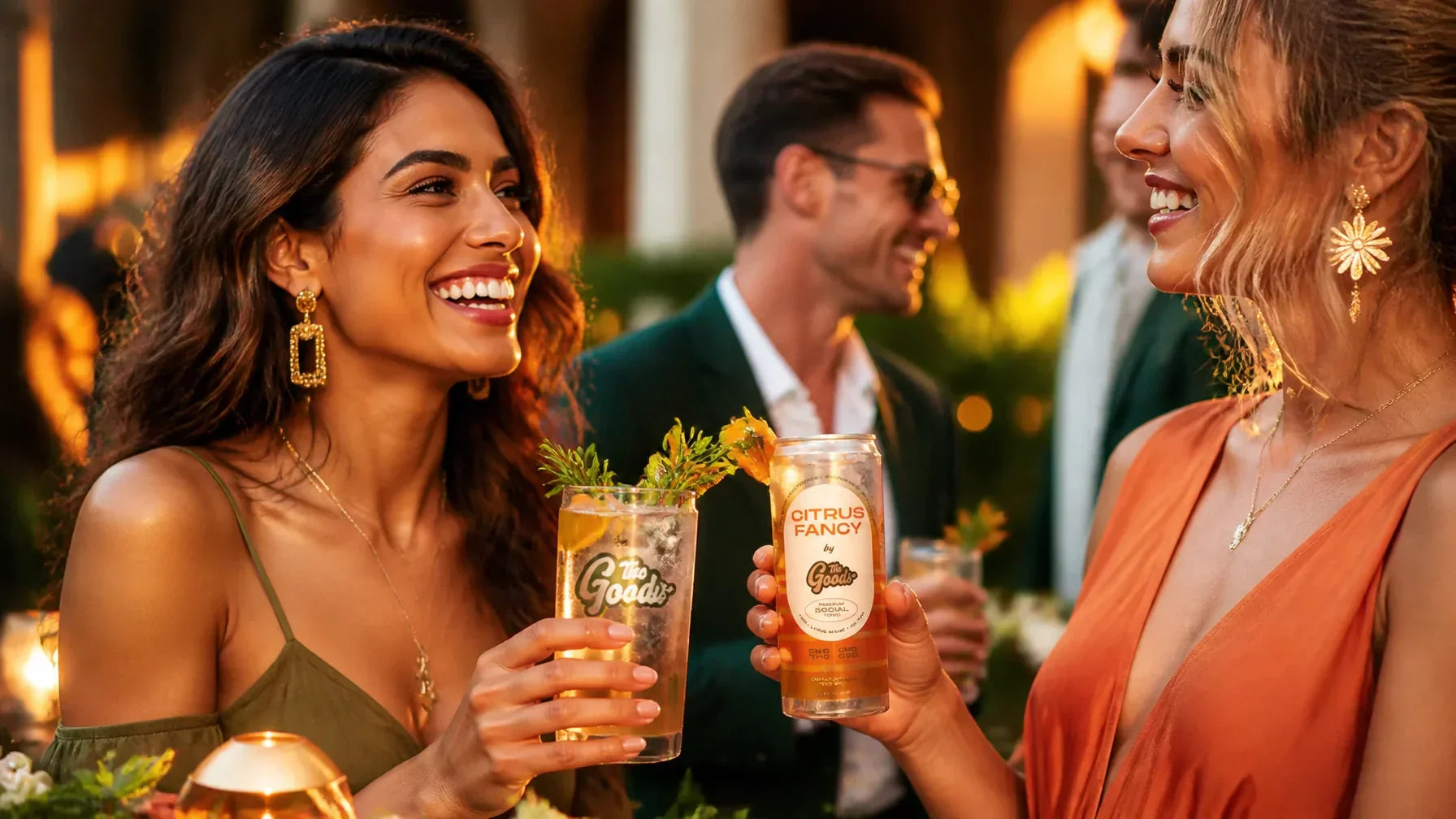 two women holding citrus fancy cocktails from The Goods in a luxury social setting