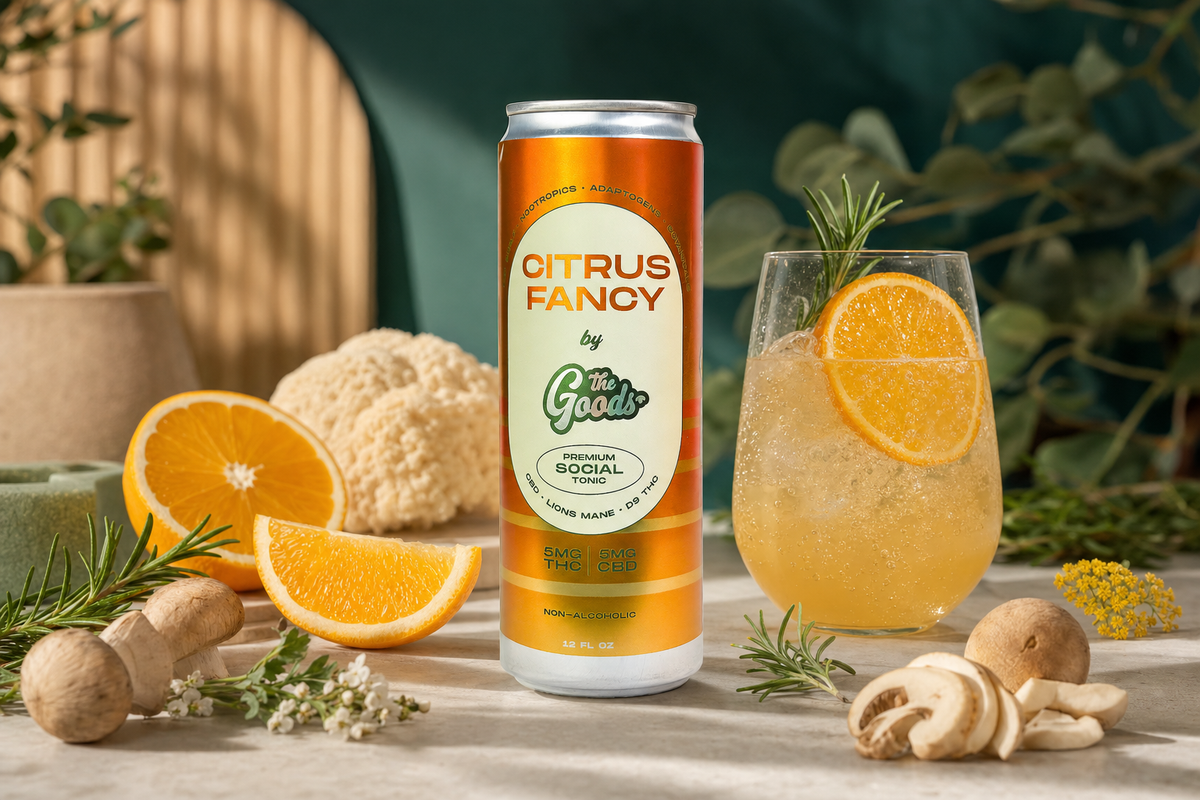 Orange "Citrus Fancy by The Goods" THC-CBD tonic can beside a garnished cocktail, oranges, mushrooms, and rosemary.