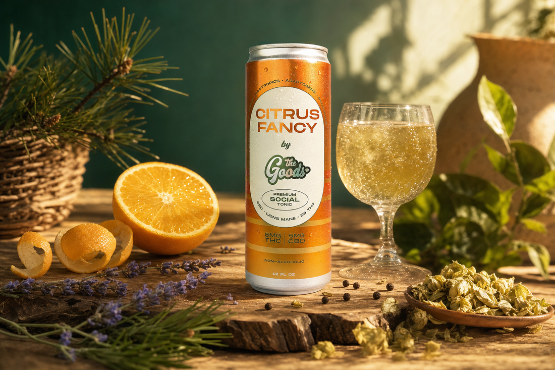 Orange "Citrus Fancy" social tonic can beside a sparkling drink, halved orange, lavender, and dried hops on wood.
