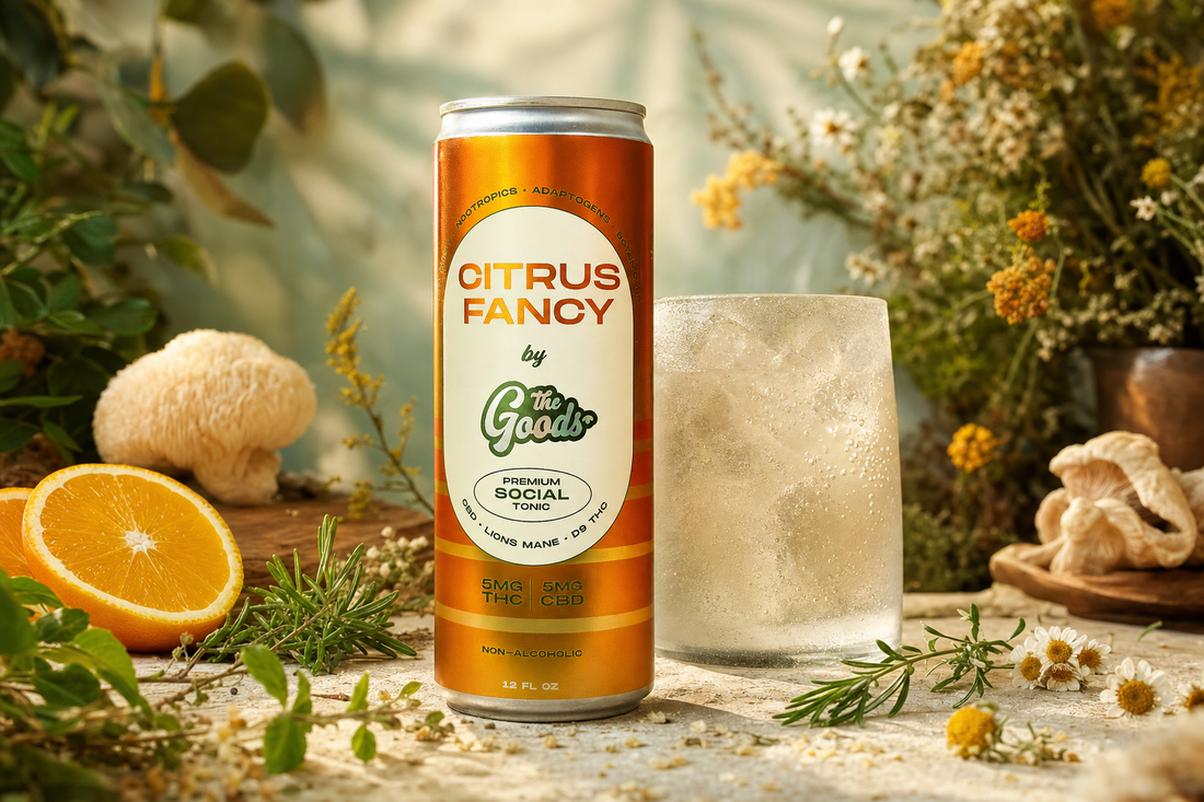 Orange "Citrus Fancy" social tonic can beside an iced glass, surrounded by orange slices, mushrooms, herbs, and flowers.