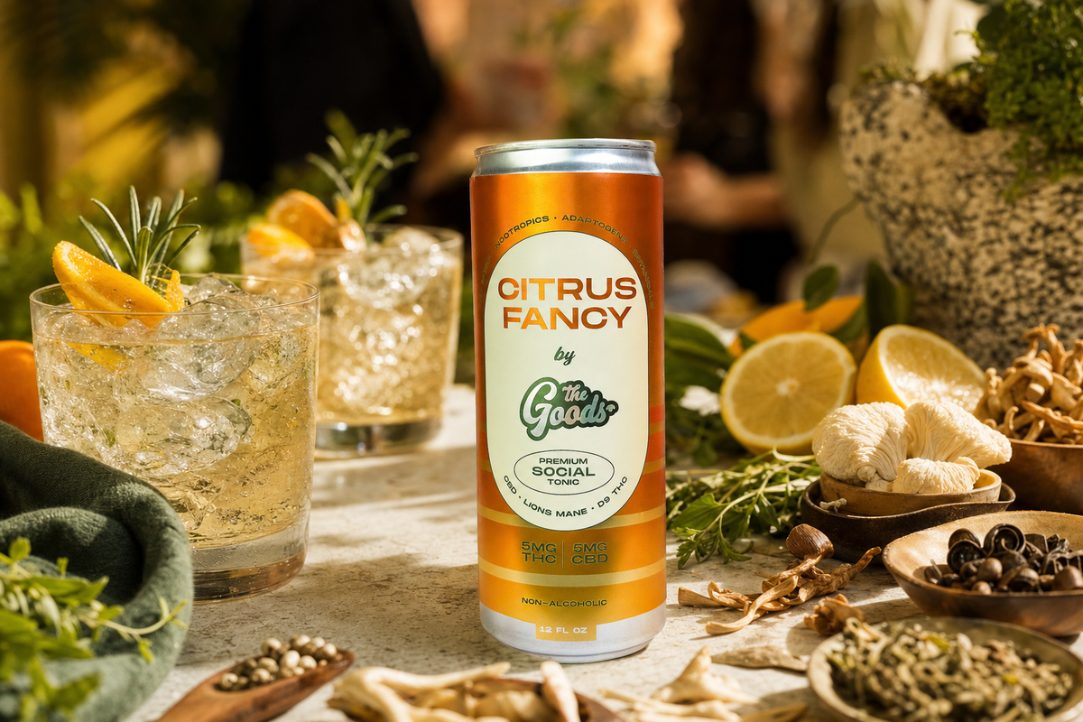 Orange "Citrus Fancy" social tonic can beside iced garnished cocktails, mushrooms, herbs, and lemons on a table.