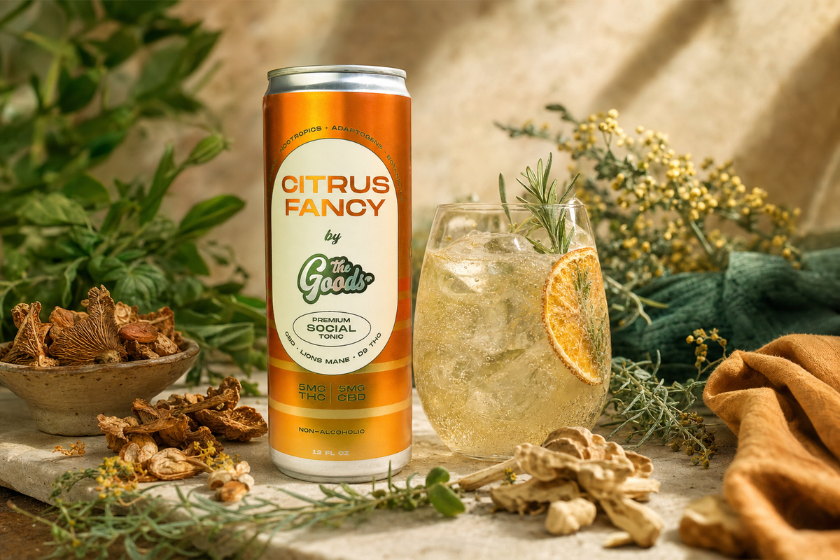 Orange "Citrus Fancy" THC/CBD social tonic can beside an iced drink garnished with rosemary and orange, among herbs and dried mushrooms.