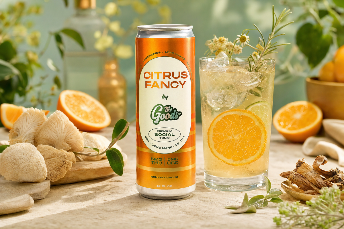 Orange "Citrus Fancy by The Goods" THC/CBD tonic can beside an iced citrus drink, mushrooms, oranges, and herbs.