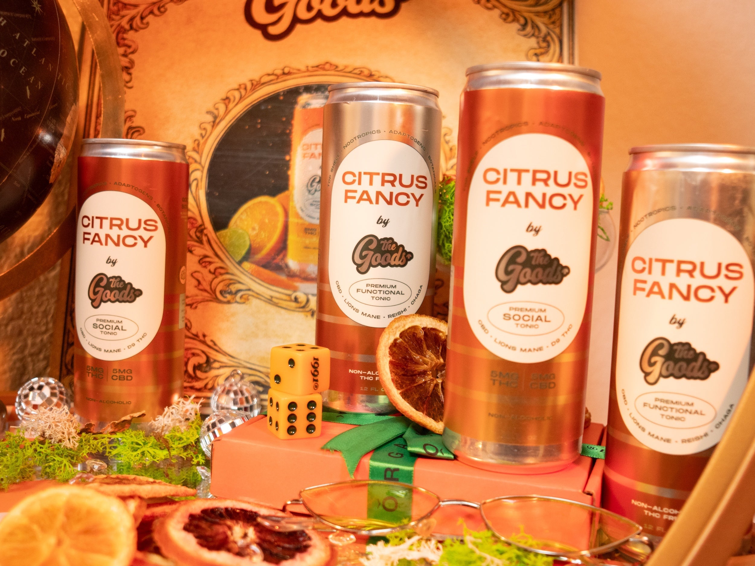 a group of orange cans in front of a branded background surrounded by branded accessories like dice and orange slices