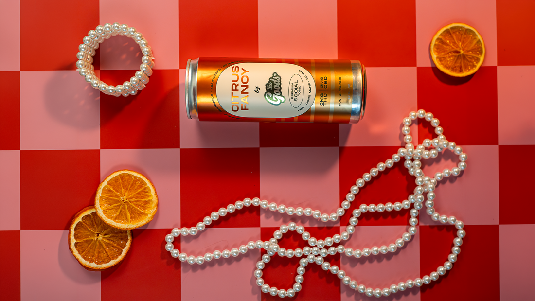 A citrus fancy can on a red and pink background laying next to orange slices and pearls
