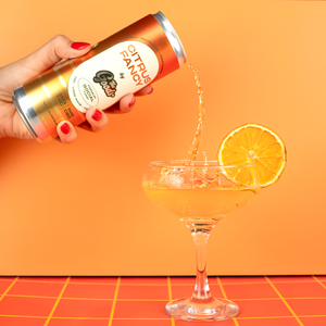 Hand pouring a can of 'Citrus Fancy' into a glass with an orange background