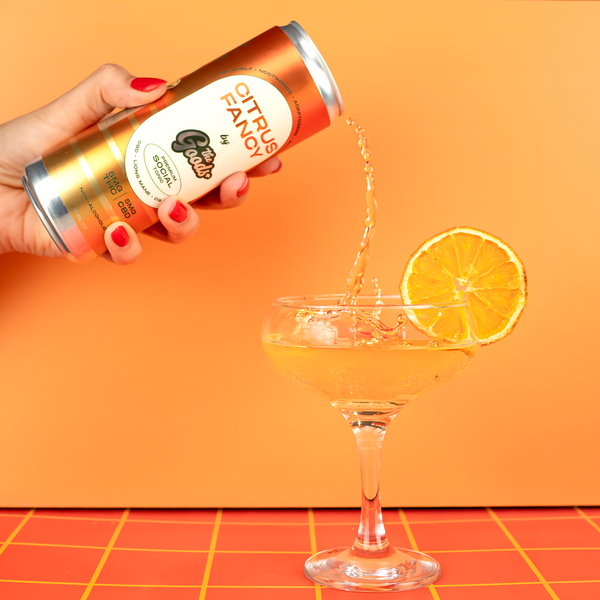 Hand pouring a can of 'Citrus Fancy' into a glass with an orange background